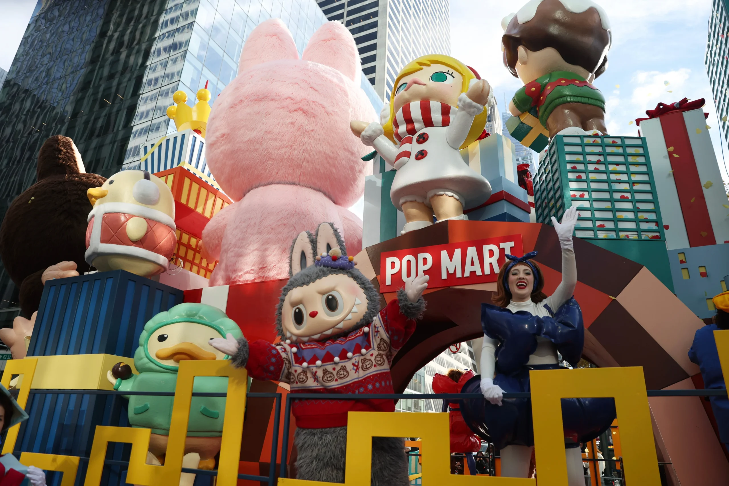 A colorful Pop Mart parade float in a city featuring giant figures of Molly, Labubu, and other characters alongside costumed performers.