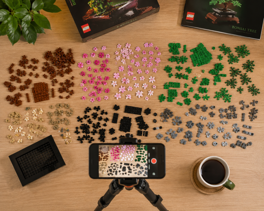 Overhead layout shot of unsorted LEGO pieces organized by color alongside an iPhone on a tripod