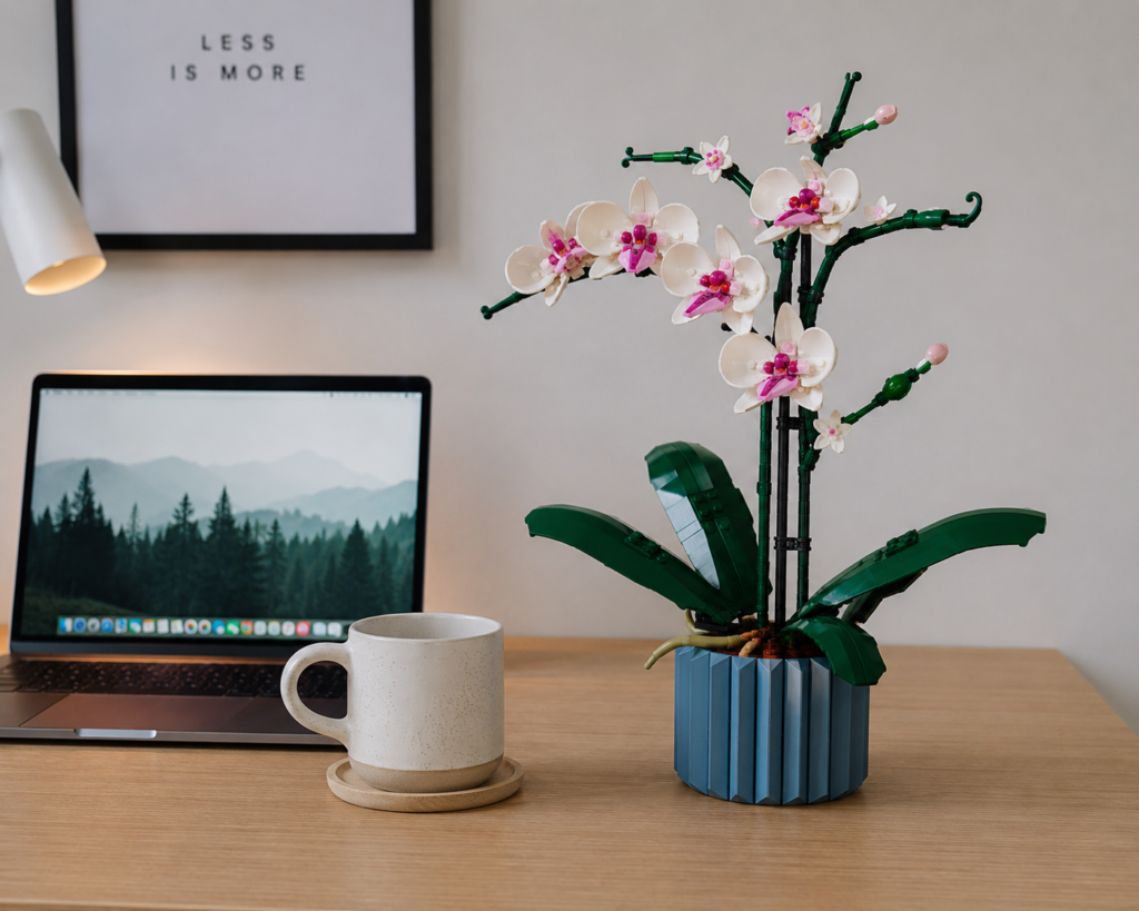 A modern minimalist desk setup featuring a fully assembled LEGO Orchid next to a laptop and a ceramic coffee mug