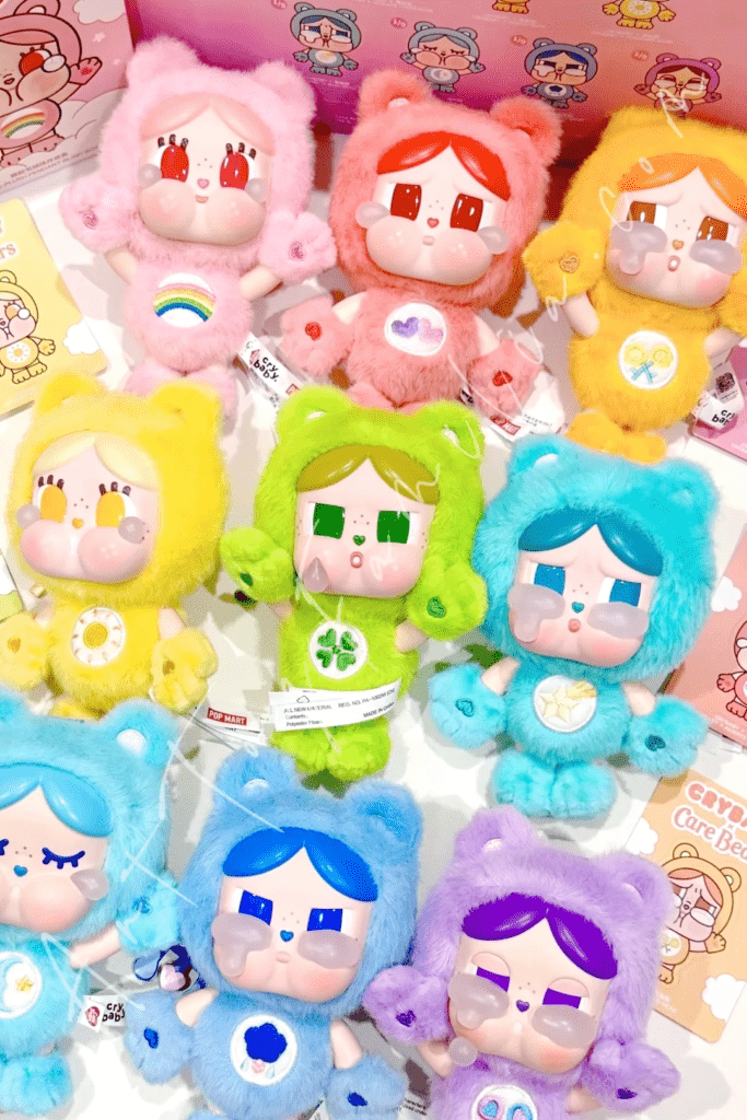 A collection of colorful Pop Mart x Crybaby x Care Bears plush pendant dolls featuring crying expressions and bear suits.