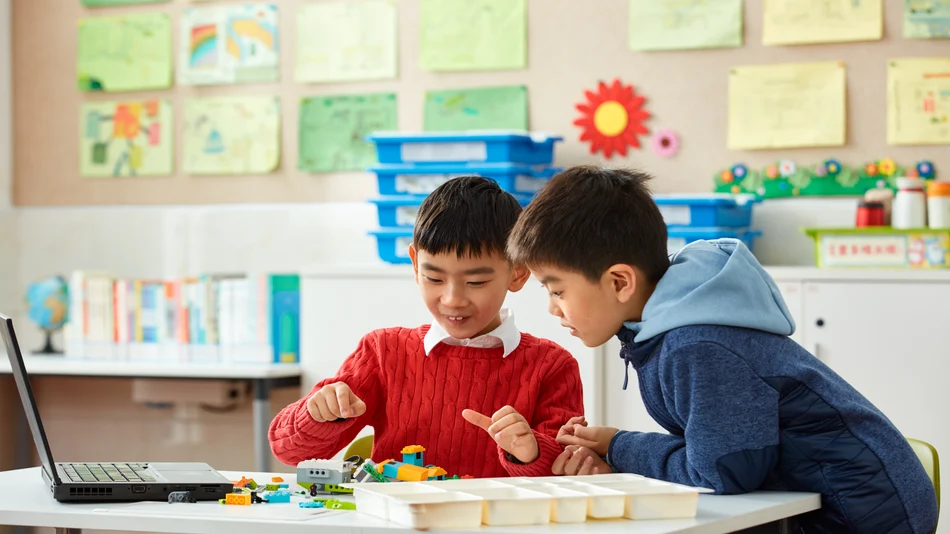Two children sitting at a classroom table, working together on a colorful LEGO building project.